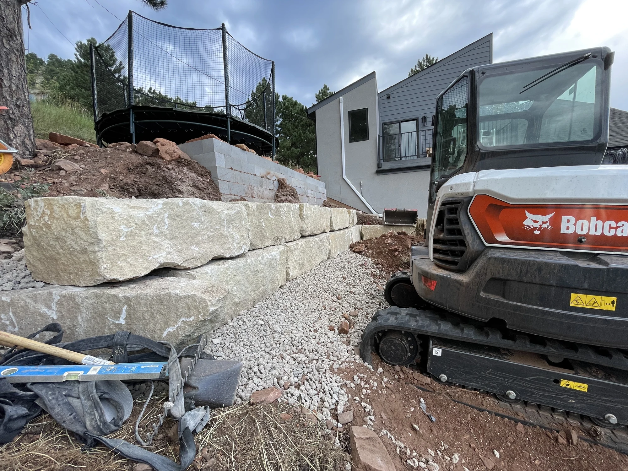 Limestone retaining wall installation beside compact equipment