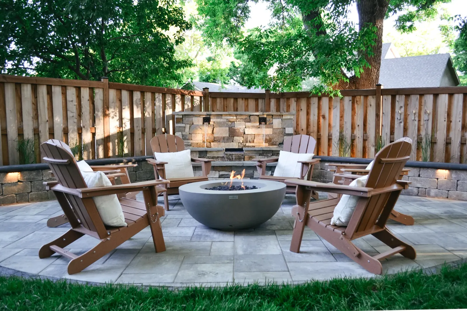 Finished circular fire pit terrace with timber seating, a stone water feature, and integrated lighting