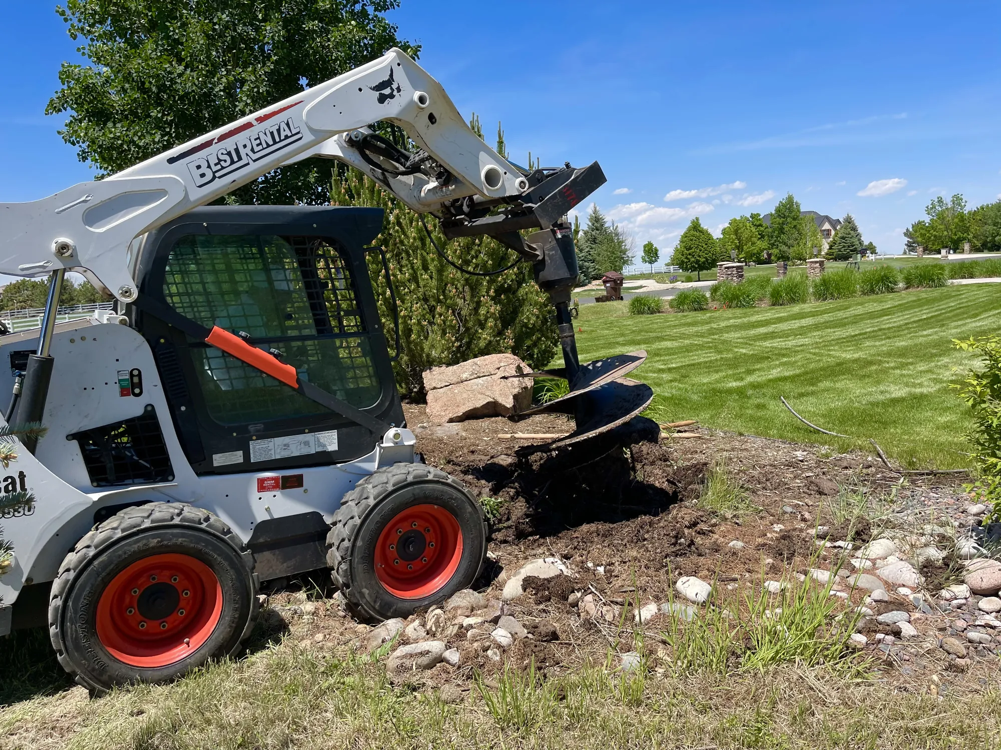 Skid-steer auger operating during landscape installation