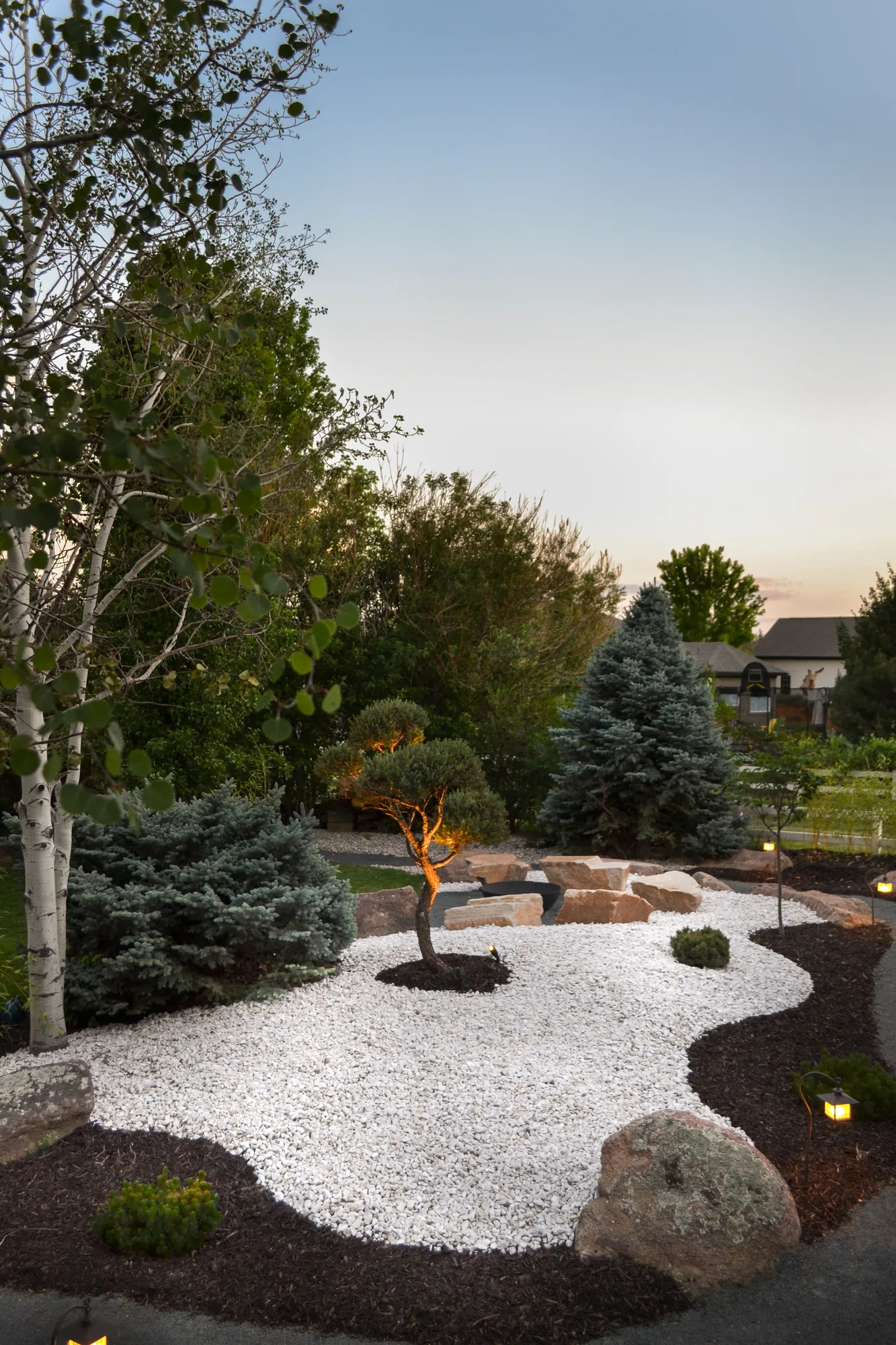 White gravel garden framed by boulders and sculptural trees